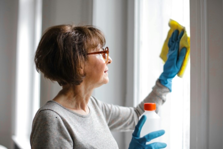 donna con capelli corti e occhiali che pulisce vetri finestre