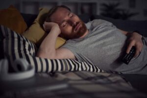 Uomo dorme sul letto con telecomando in mano