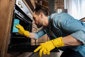uomo con guanti gialli che pulisce il forno con straccio azzurro