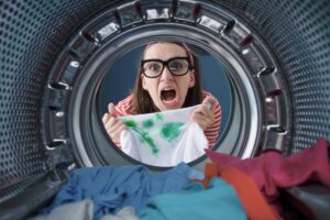 Ragazza disperata vista oblo della lavatrice con una maglia macchiata in mano