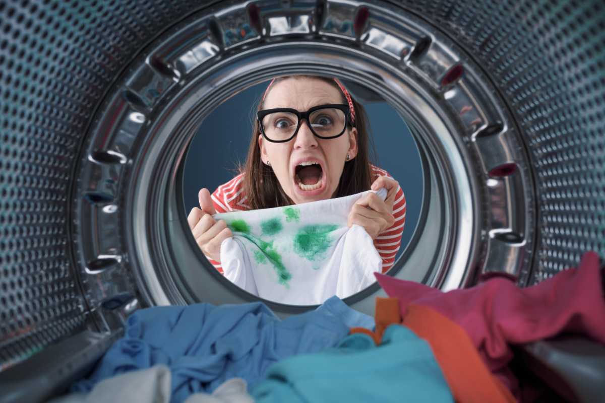 Ragazza disperata vista oblo della lavatrice con una maglia macchiata in mano