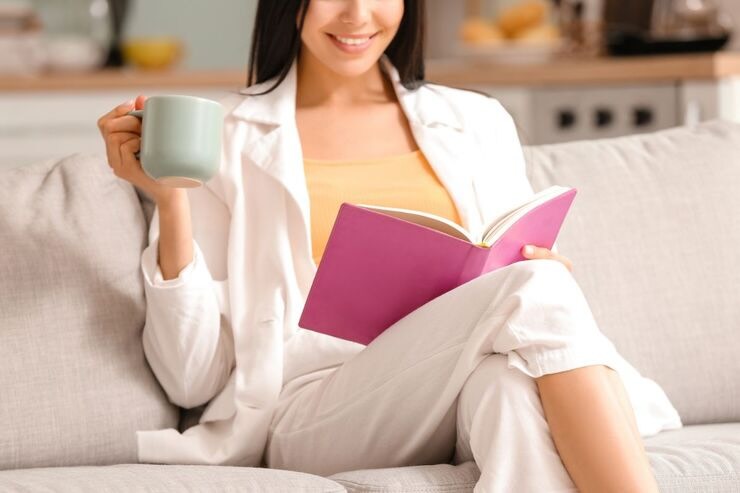 Ragazza seduta sul divano con tazza verde legge da un libro con copertina fucsia