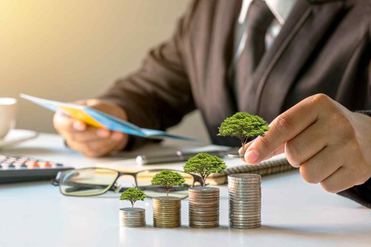 Uomo che impila monete con mini alberi di sopra