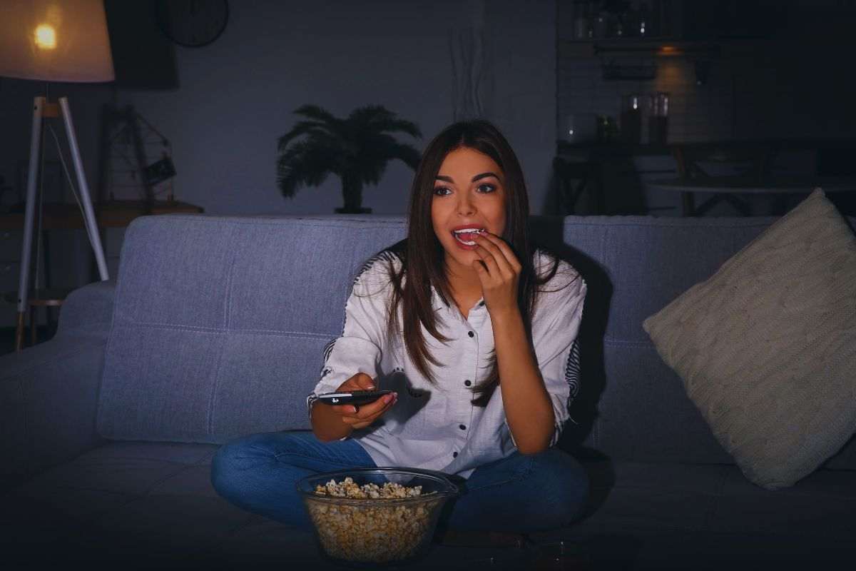 Ragazza seduta su divano che mangia pop corn
