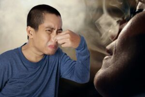 Ragazzo infastidito dall'odore di fumo, sullo sfondo una donna che fuma