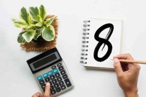 persona che usa calcolatrice e scrive numero otto su un taccuino