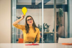 Ragazza con maglione giallo alza la mano ed ha una lampadina disegnata