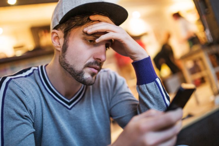 uomo con il cellulare in mano e con l'altra mano sulla fronte e l'espressione preoccupata