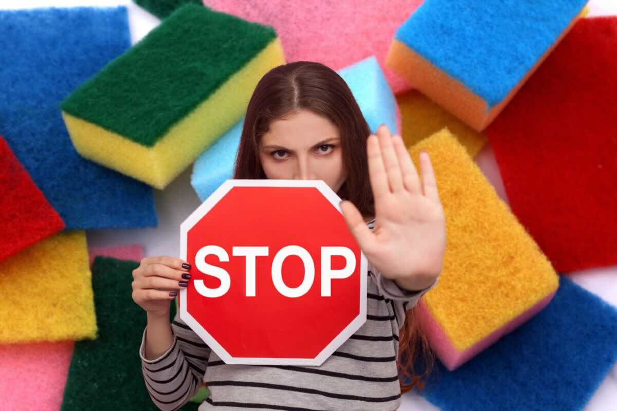 Donna con cartello stop e mano che blocca e sul fondo spugne da cucina colorate