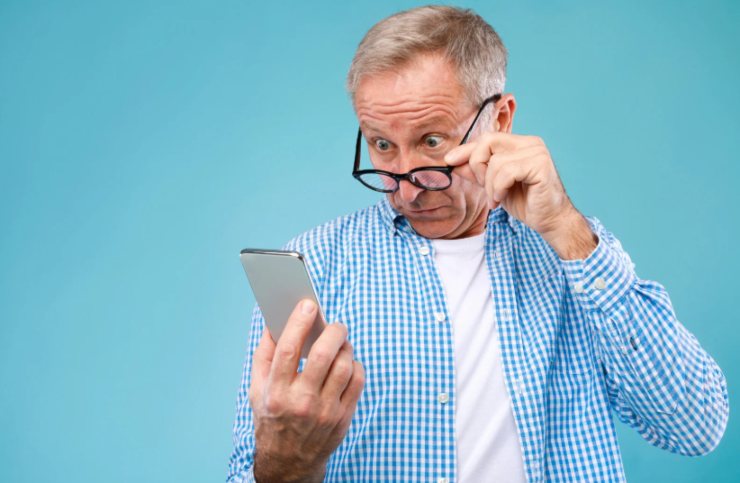 uomo che guarda il cellulare e si tocca gli occhiali con una mano