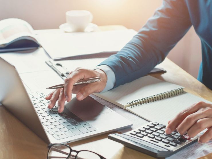 persona fa calcoli alla scrivania con pc e calcolatrice