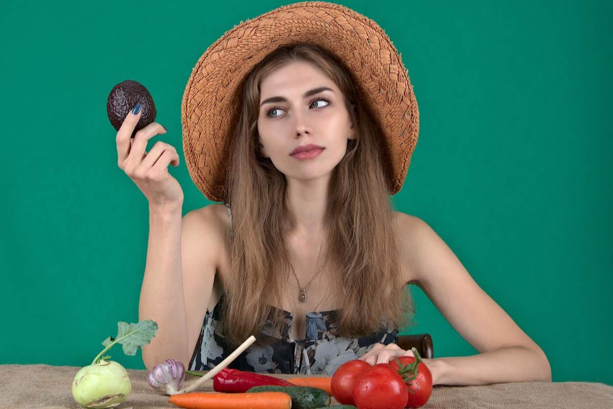 donna con in mano un avocado e davanti a sé degli ortaggi su un tavolo