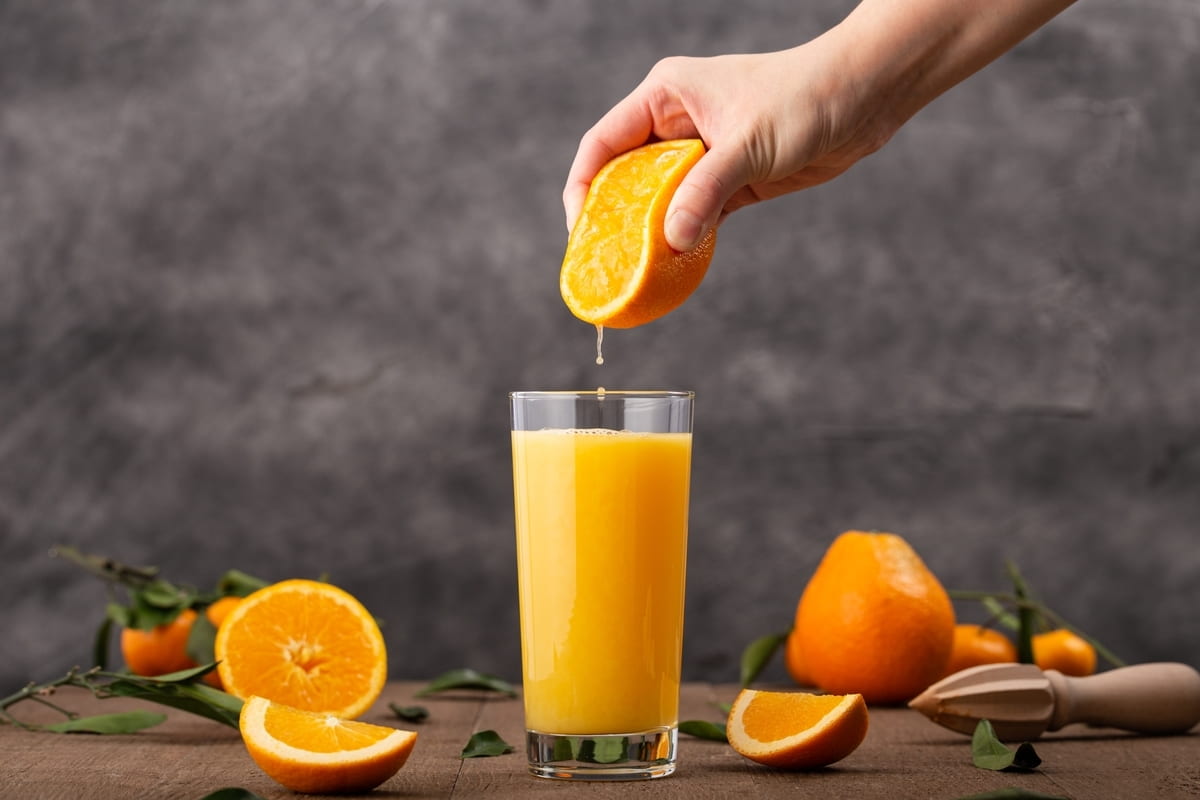 mano che spreme un'arancia sopra un bicchiere di succo