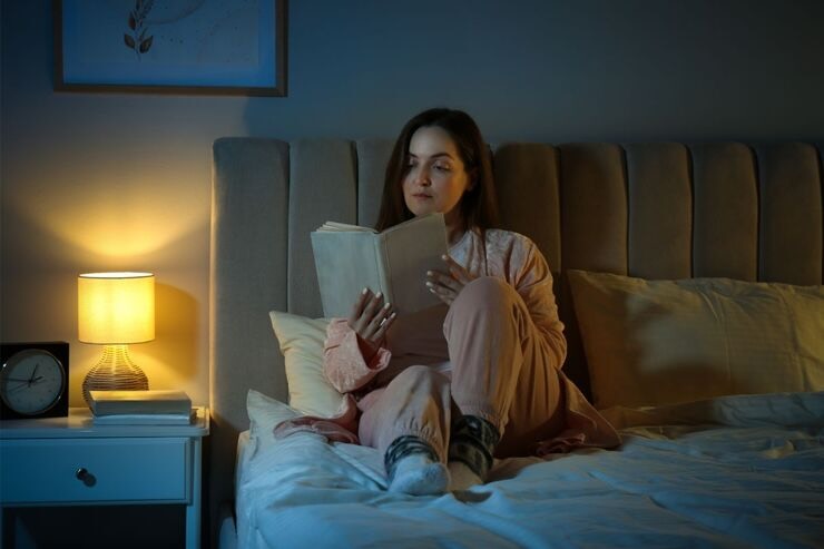 Donna legge libro luce soffusa sul letto