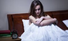 Ragazza sul letto contrariata guarda sveglia che segna le 3