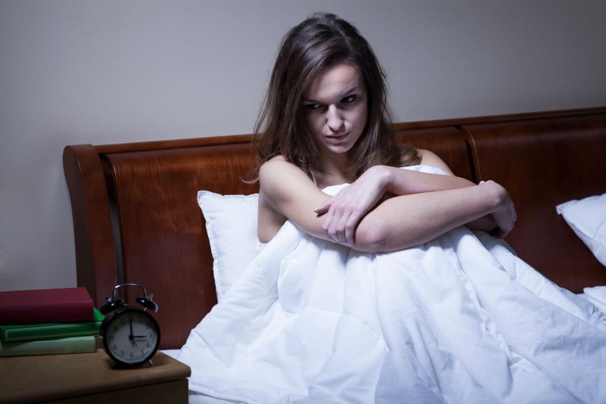 Ragazza sul letto contrariata guarda sveglia che segna le 3