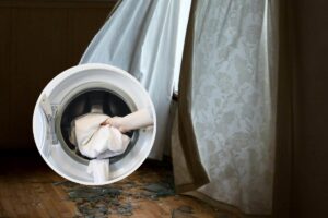 Delle tende bianche e, in evidenza, un oblò di una lavatrice