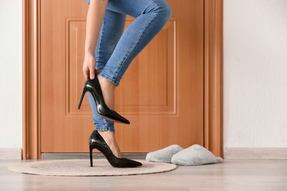Gambe di donna con jeans che toglie scarpe con tacchi, ciabatte di lato