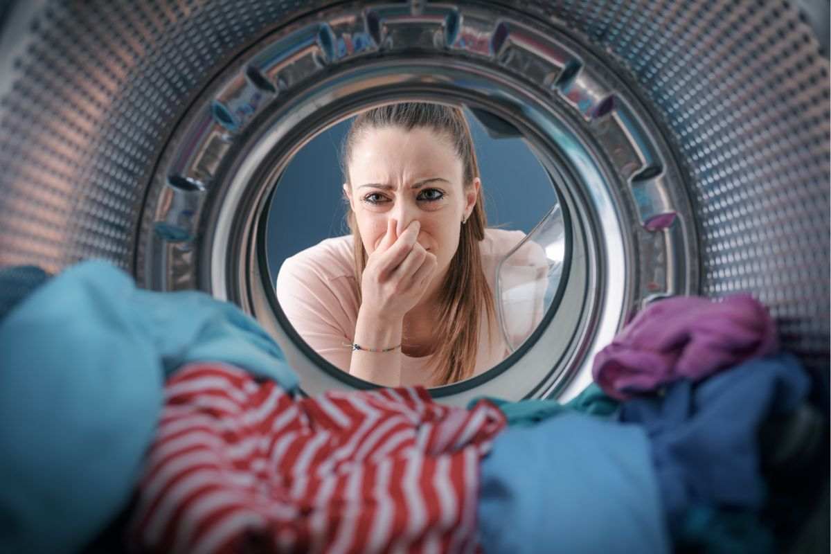 Donna che si tiene il naso per non sentire la puzza che esce dalla lavatrice