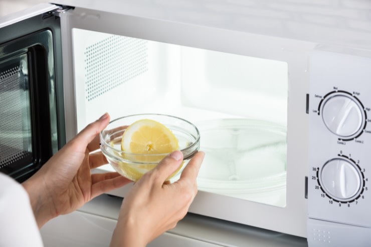 mani che mettono scodella con limone nel microonde