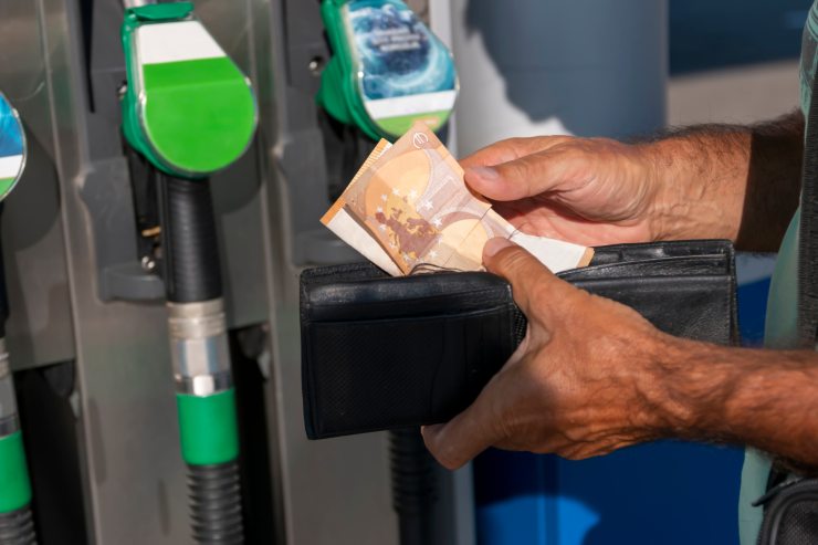 Uomo che tira fuori le banconote da 50€ davanti ad un distributore di benzina