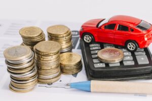 Pila di monete accanto a calcolatrice e modellino di auto