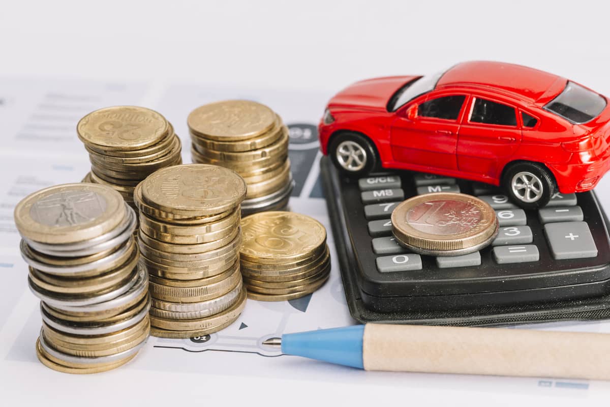 Pila di monete accanto a calcolatrice e modellino di auto