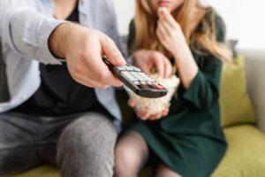 Un uomo e una donna seduti sul divano. Lui con telecomando e lei con popcorn