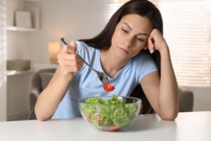 Donna con aria triste davanti ad una ciotola d'insalata