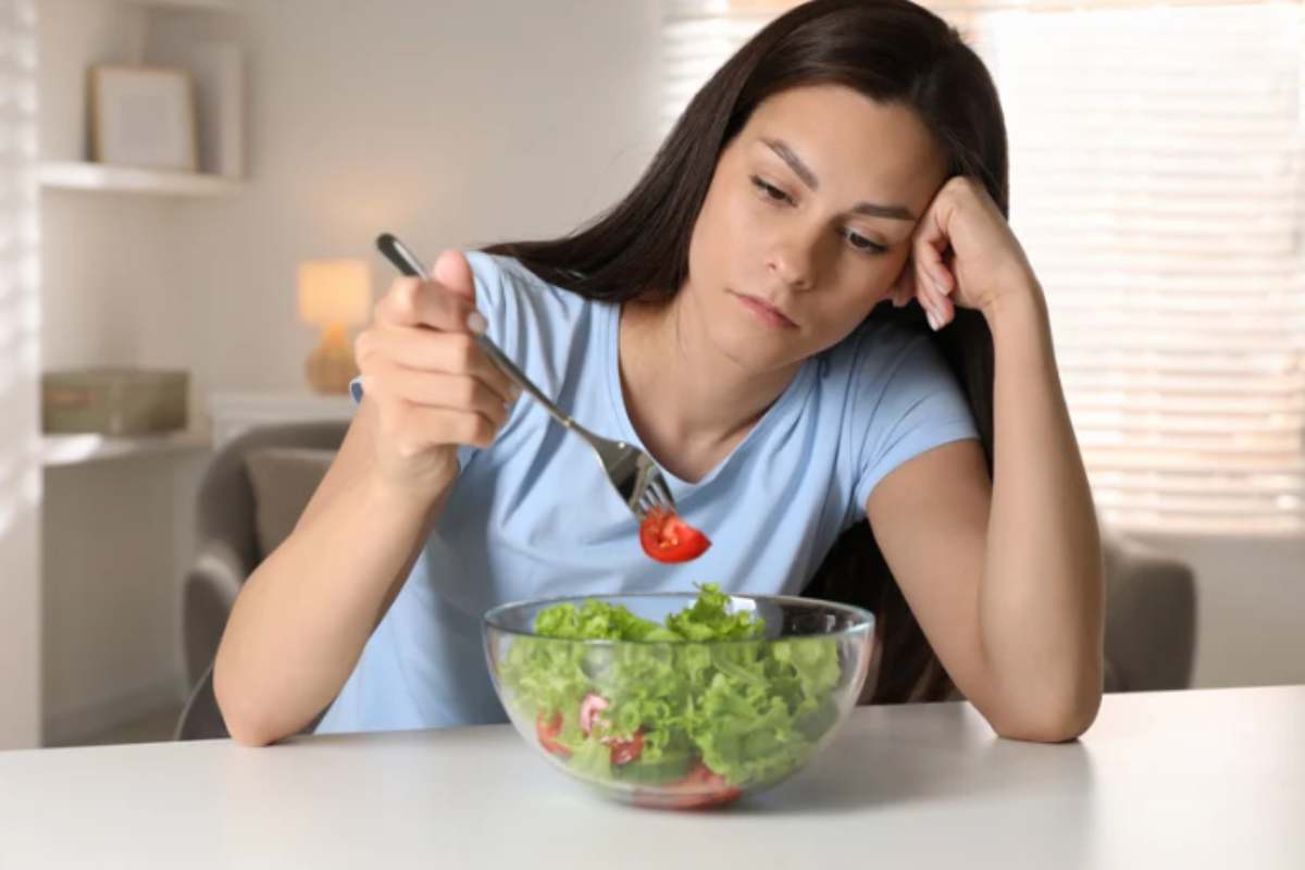 Donna con aria triste davanti ad una ciotola d'insalata