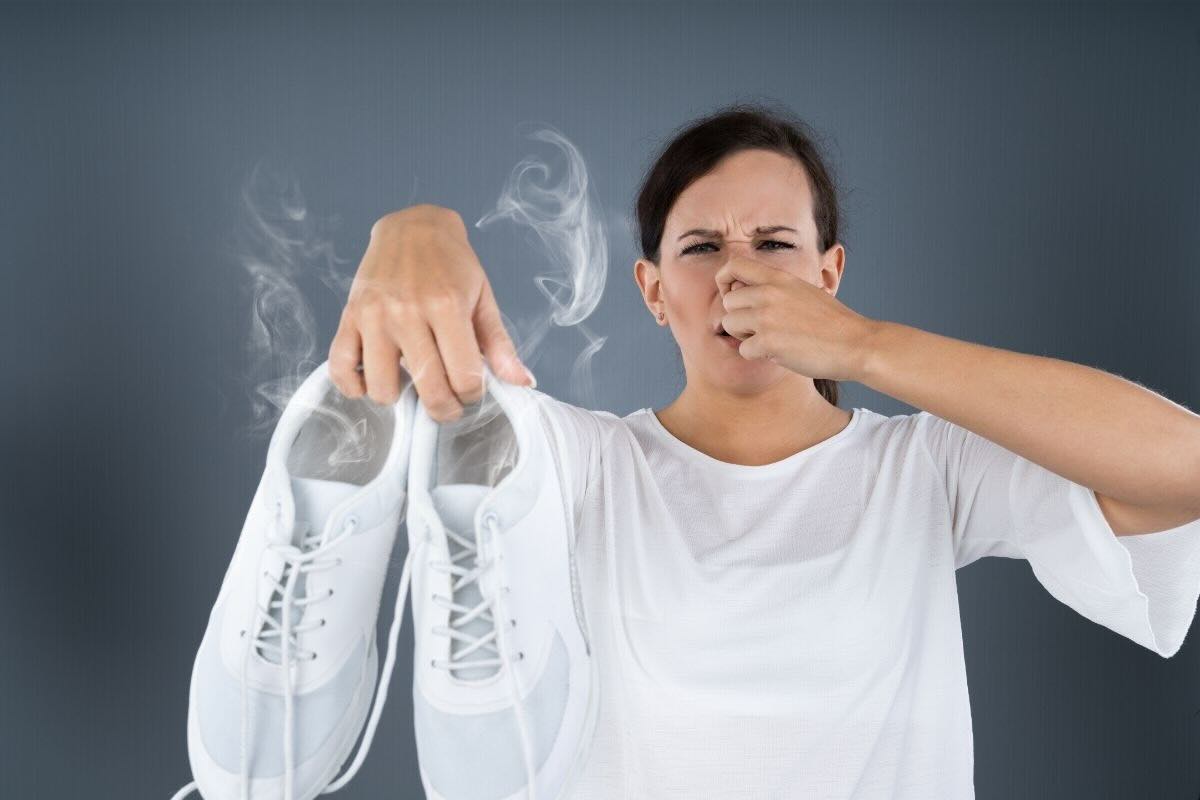 Donna tiene in mano scarpe bianche che puzzano