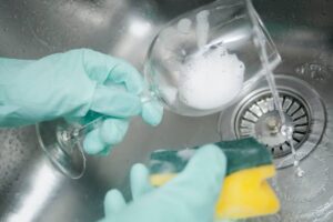 Persona che lava bicchiere con detersivo e spugna