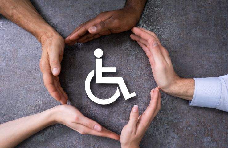 mani che proteggono icona di persona disabile su sedia a rotelle